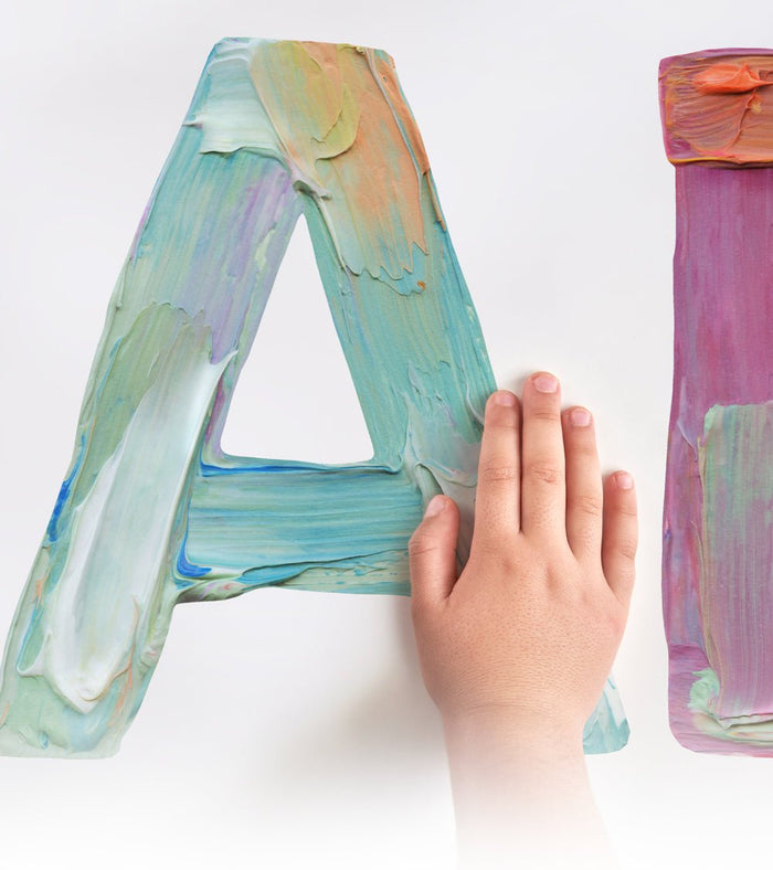 A child's hand touching a wall decal of a letter A, that looks like it is painted on the wall