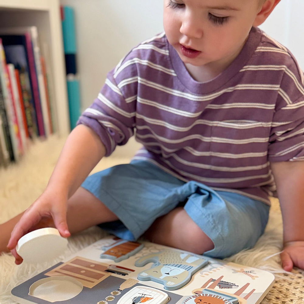Toddler places a round piece into a pet-themed chunky puzzle for toddlers; soft neutral colors and books in the background.