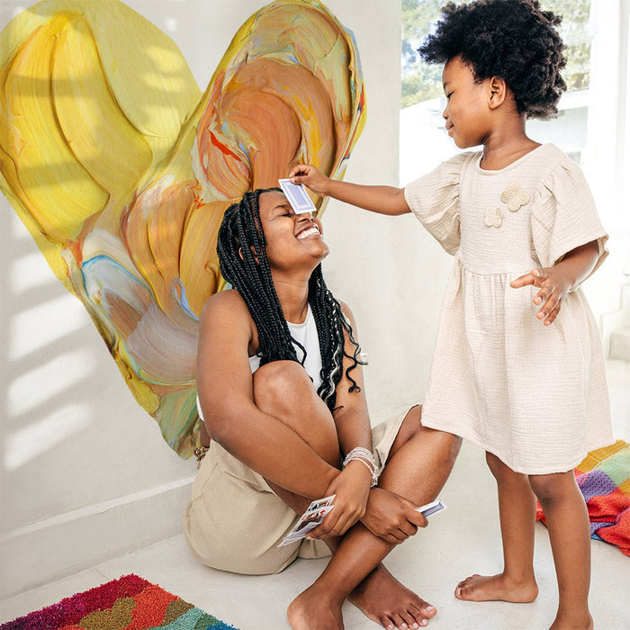 A child playing cards with her mom in front of a giant painterly Paintbox Heart Wall Decal .