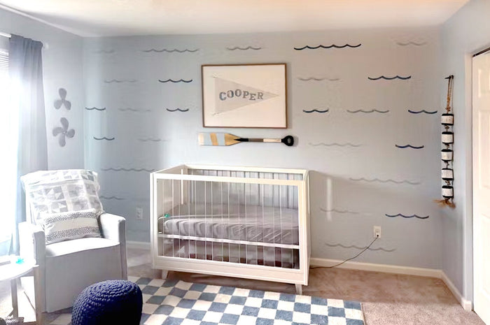 watercolor waves removable decals fill the pale blue wall behind a crib in a modern coastal baby nursery