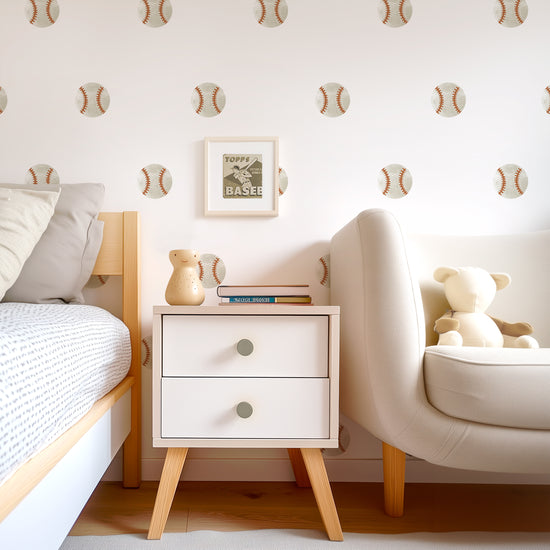 A teen room wall adorned with watercolor baseball wall decals by Mej Mej is the background for a modern chest, bed and chair. The decals are placed in an even pattern behind a small framed vintage baseball image