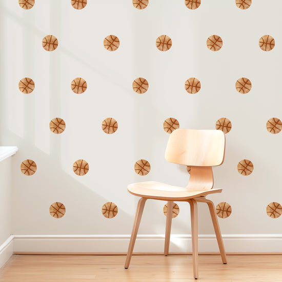 A wall is decorated with removable watercolor basketball wall decals by Mej Mej. They are placed in a grid pattern. A modern chair sits in front of them for scale.