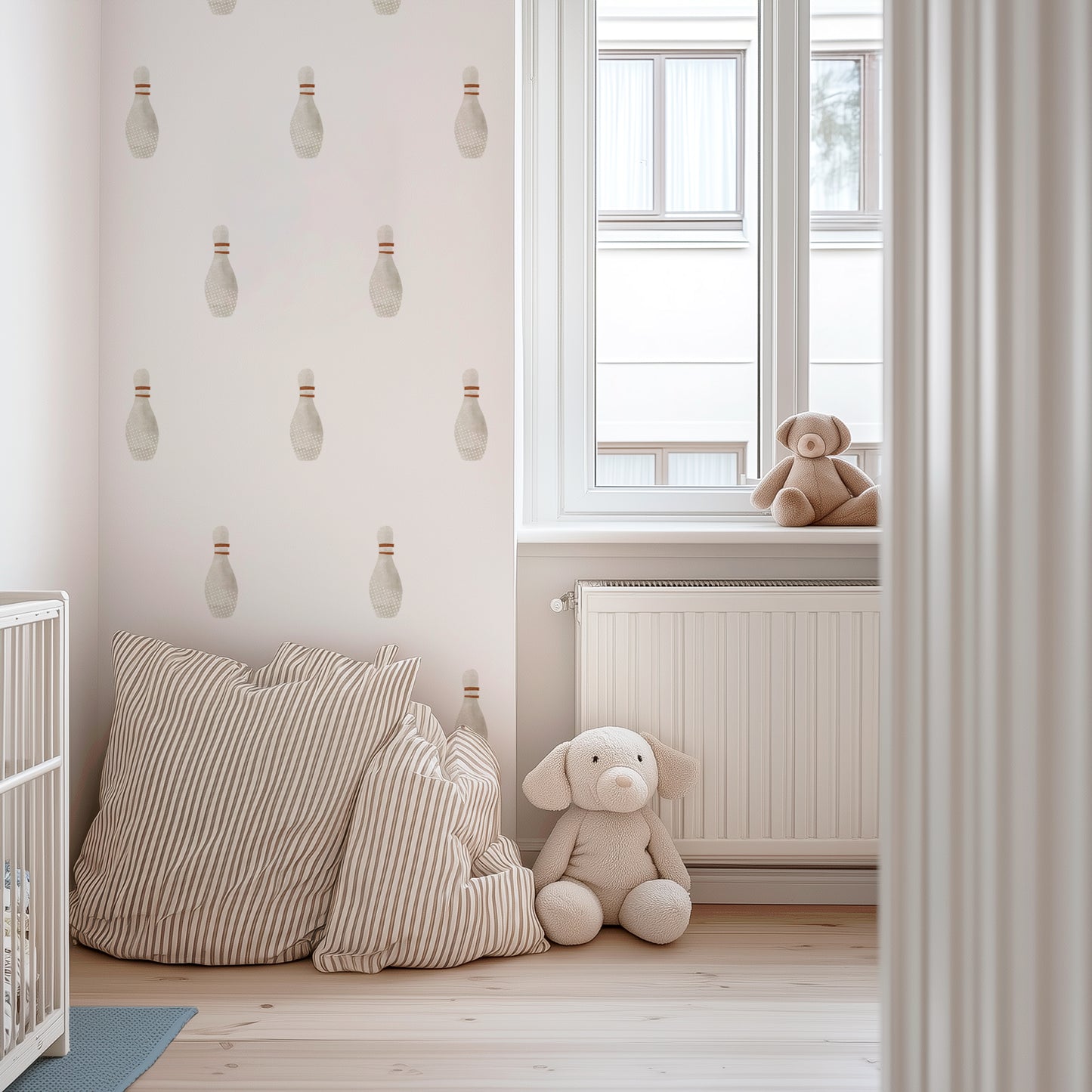 An accent wall decorated with watercolor bowling wall decals by Mej Mej is next to a window in a child’s nursery of soft muted creams with a white crib and striped floor pillows.