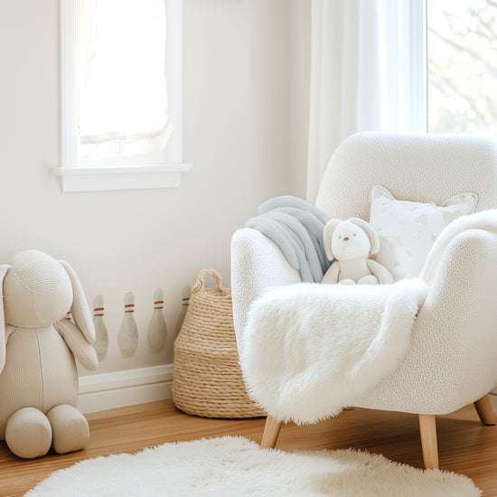 A kids’ room with Mej Mej bowling pin removable wall decals running above the baseboard tucked behind a cream reading chair and natural basket.