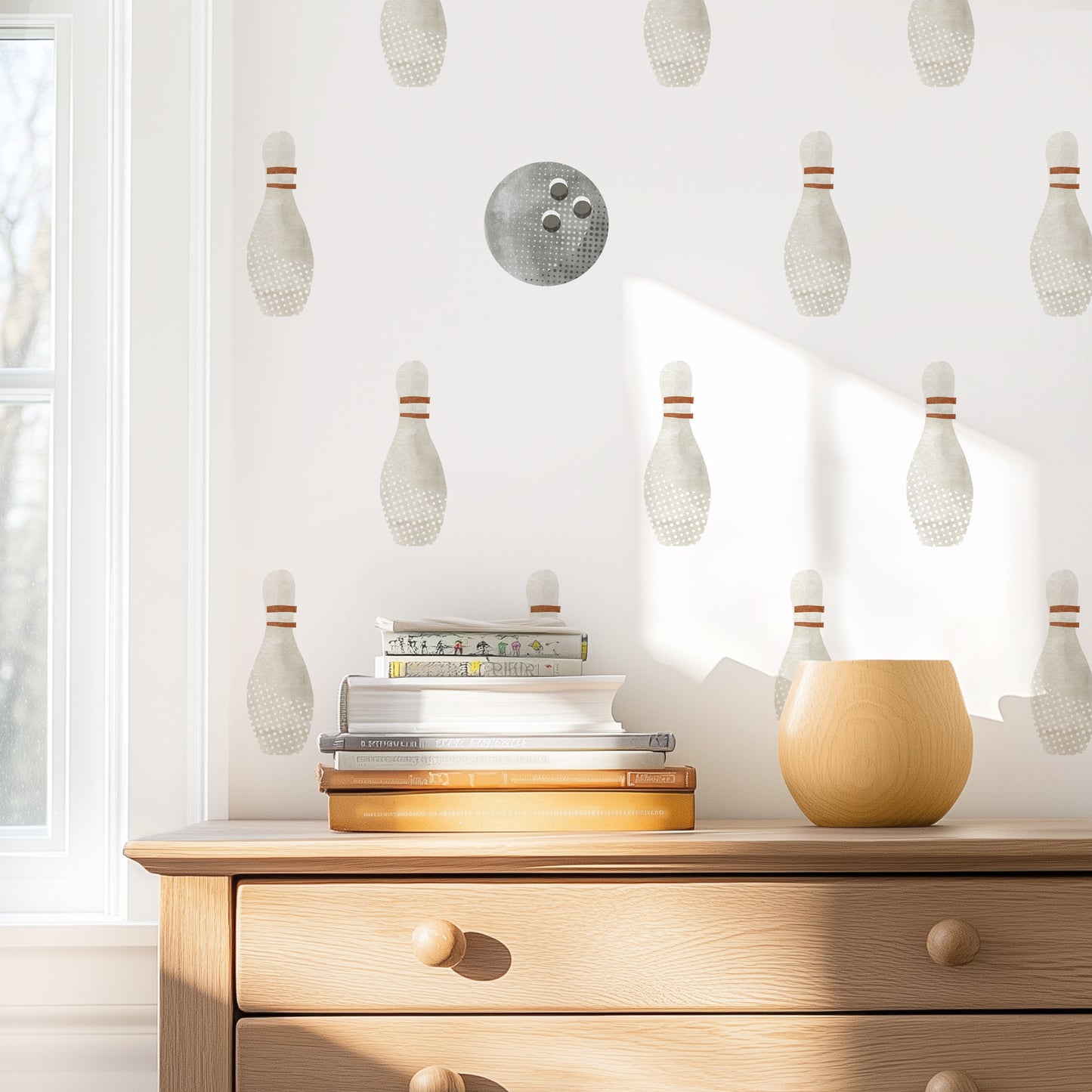 Watercolor bowling wall decals by Mej Mej on accent wall behind natural wooden chest of drawers with books stacked on top.