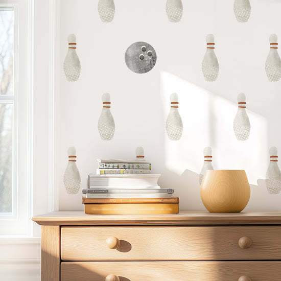 Watercolor bowling wall decals by Mej Mej on accent wall behind natural wooden chest of drawers with books stacked on top.