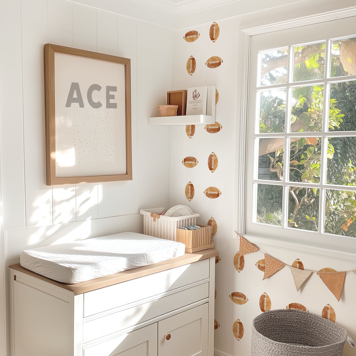 Watercolor football decals are placed in a grid pattern on an accent wall in a sunlit child’s nursery. A changing table is in front of the accent wall with a framed print that says ACE.