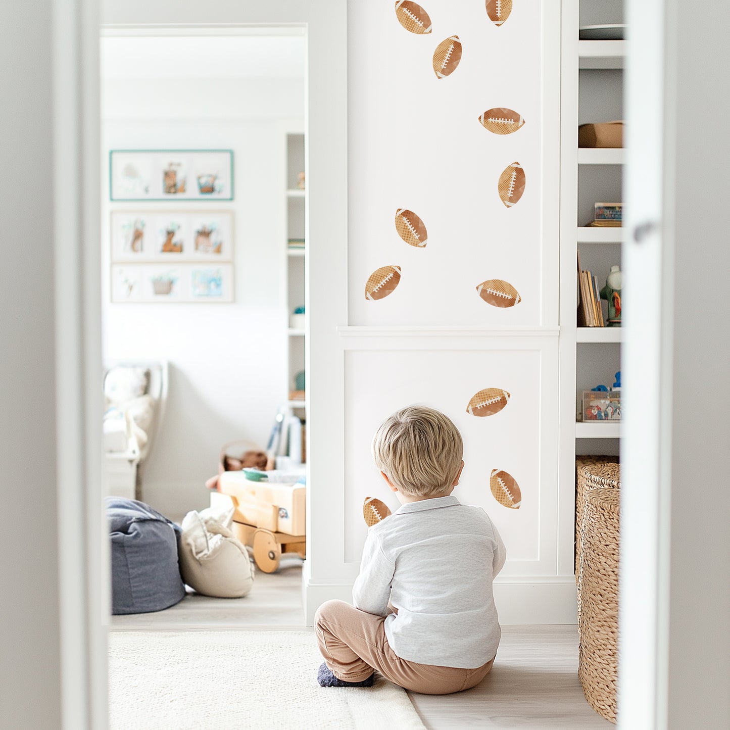 Watercolor football removable decals by Mej Mej are tossed on an accent wall in a child’s playroom. A little boy is sitting on the floor looking at them.