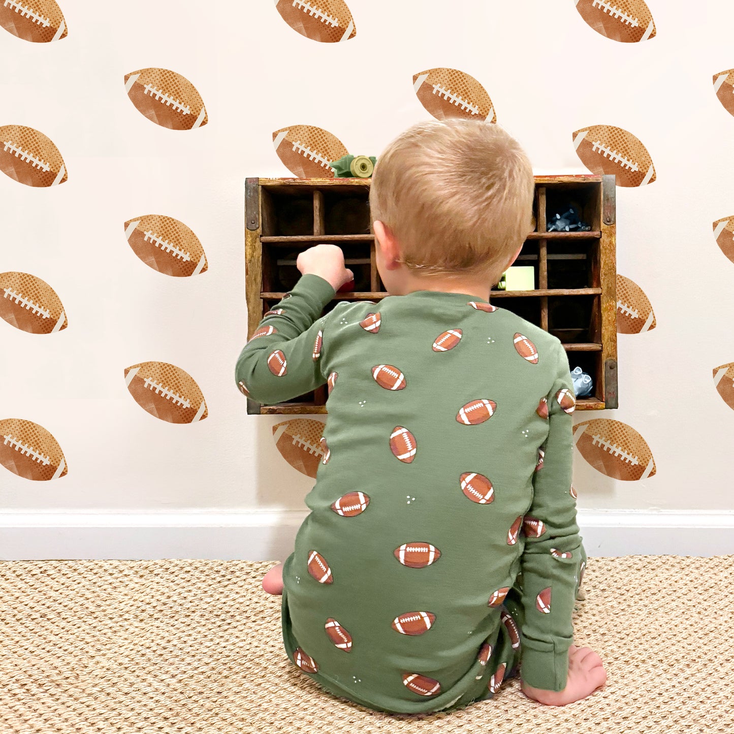 Watercolor football removable decals by Mej Mej are tossed on an accent wall in a grid pattern in a child’s playroom. A little boy is sitting on the floor playing.