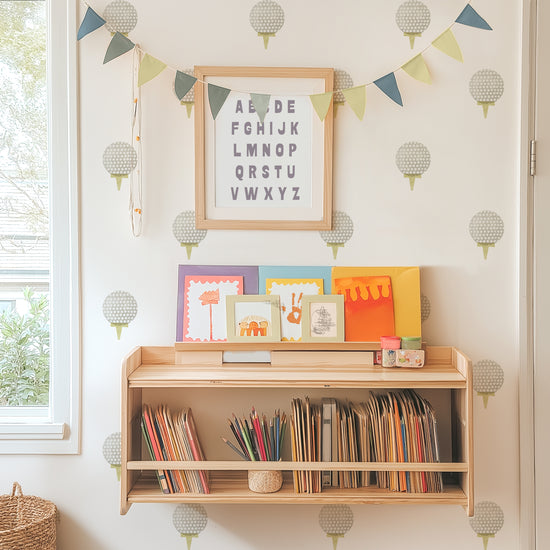 Watercolor golf ball wall decals adorn a wall behind a bookshelf with books, art supplies and kids’ artwork displayed. A framed alphabet and pennant are hung on top of decals.