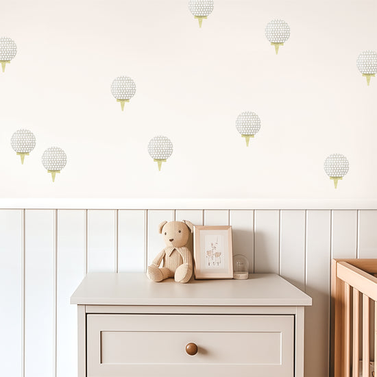 Watercolor golf ball removable decals by Mej Mej are tossed in a directional pattern on a wall in a child’s playroom. A chest and crib sit in front of a chair railing.