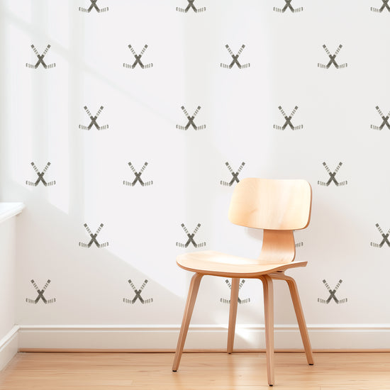 A wall is decorated with watercolor crossed hockey sticks removable fabric wall decals by Mej Mej. They are placed in a modern grid pattern. A mid-century chair sits in front of them for scale.