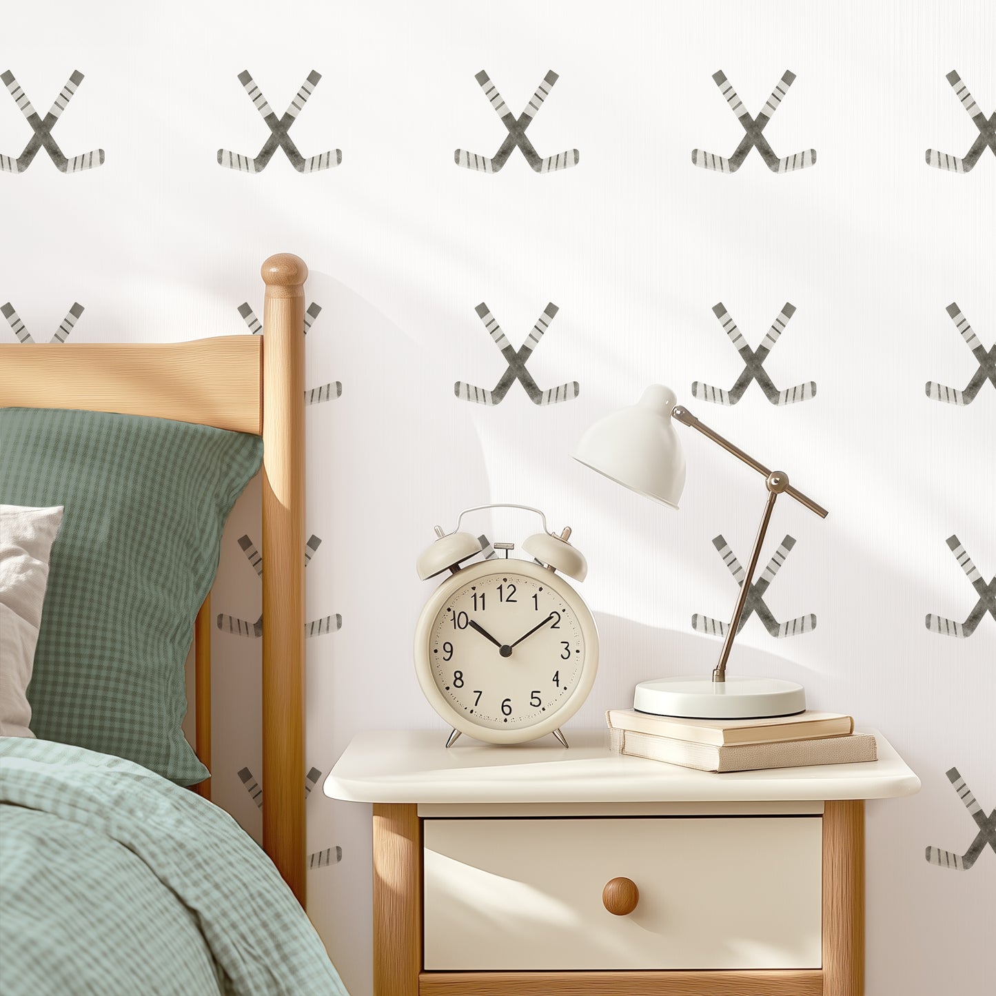 A white wall with crossed hockey sticks fabric decals placed in a grid pattern is the backdrop for a stylish bedroom. A bed with coordinating bedding, a nightstand with an oversized vintage alarm clock and gooseneck lamp complete the modern vibe.