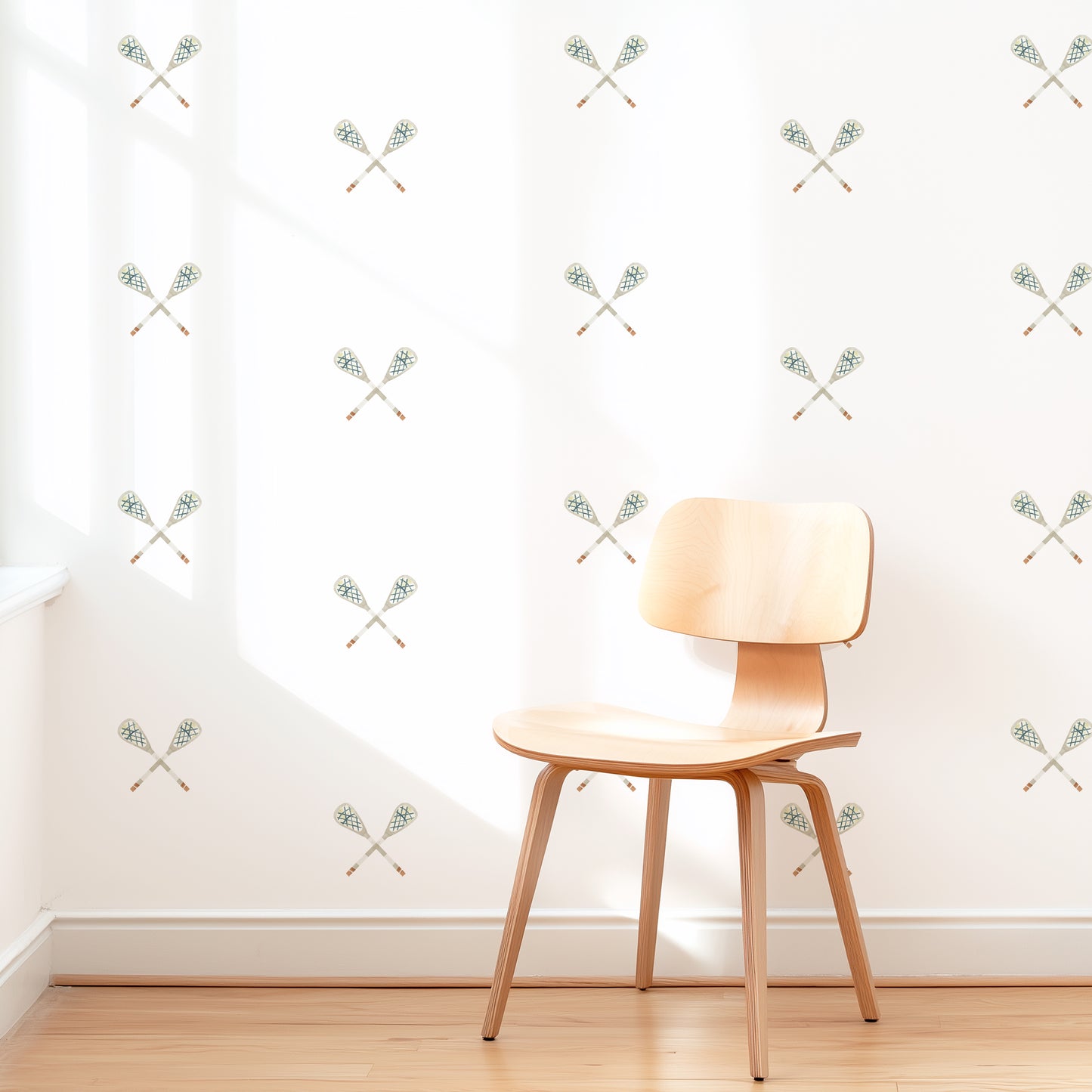 A wall is decorated with watercolor crossed lacrosse sticks removable fabric wall decals by Mej Mej. They are placed in a modern grid pattern. A mid-century chair sits in front of them for scale.