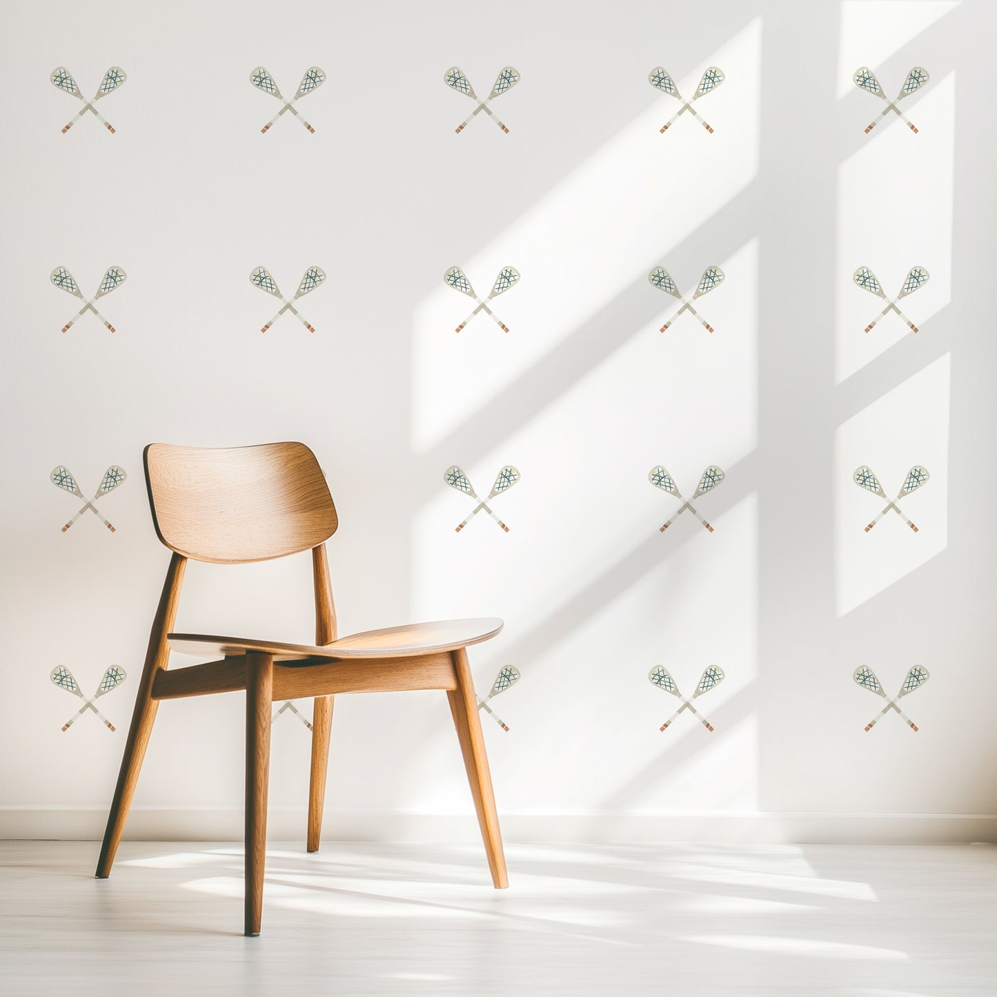 A wall is decorated with watercolor crossed lacrosse sticks removable fabric wall decals by Mej Mej. They are placed in a modern grid pattern. A modern chair sits in front of them for scale.