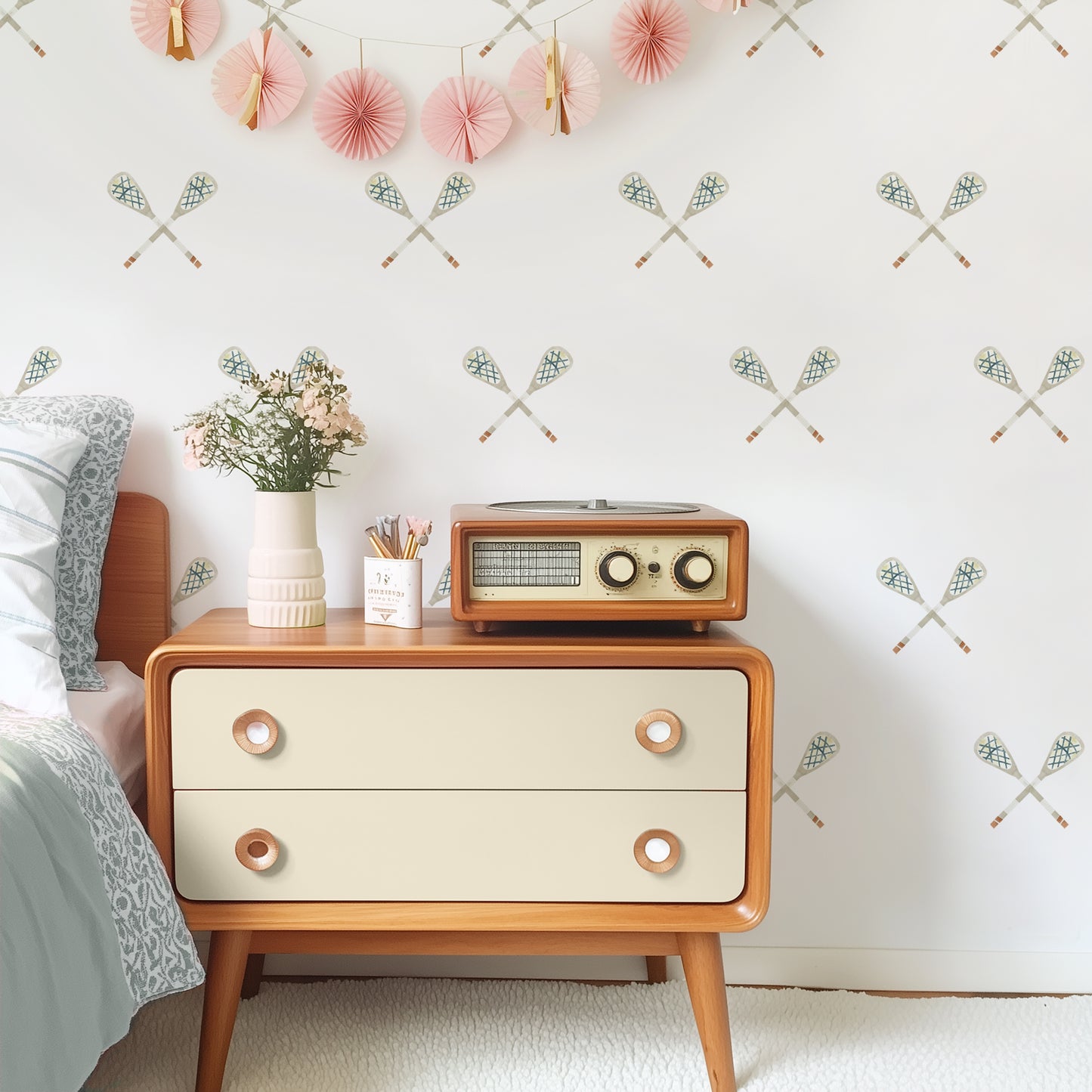 A tween room features wall decals with muted watercolor crossed lacrosse sticks by Mej Mej. A vintage chest and radio are styled for a modern look.