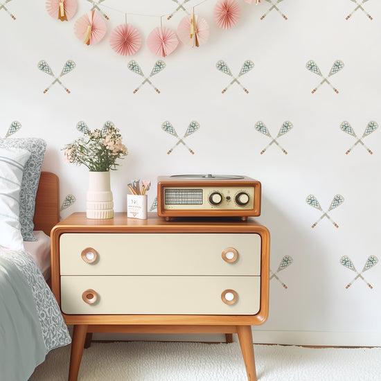 A tween room features wall decals with muted watercolor crossed lacrosse sticks by Mej Mej. A vintage chest and radio are styled for a modern look.