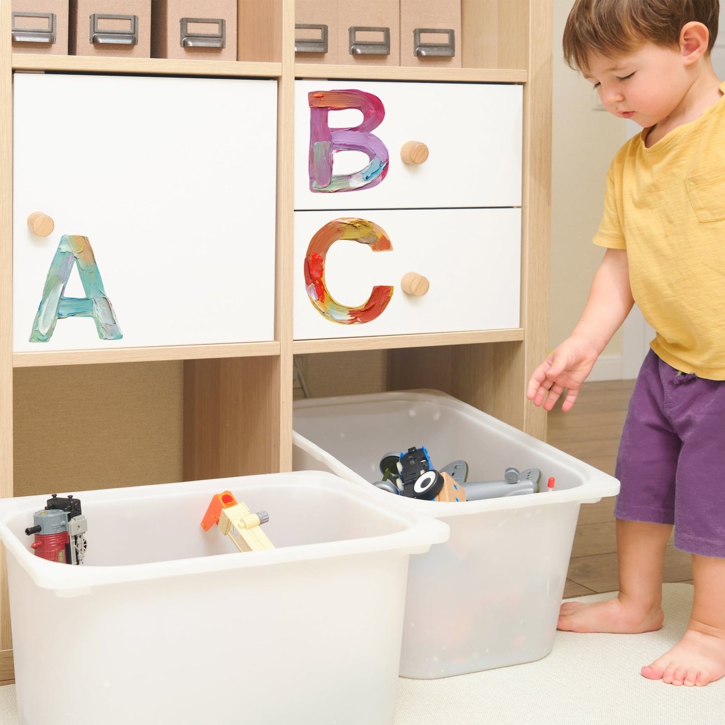 Child playing near storage bins labeled with colorful peel-and-stick alphabet wall decals for organization