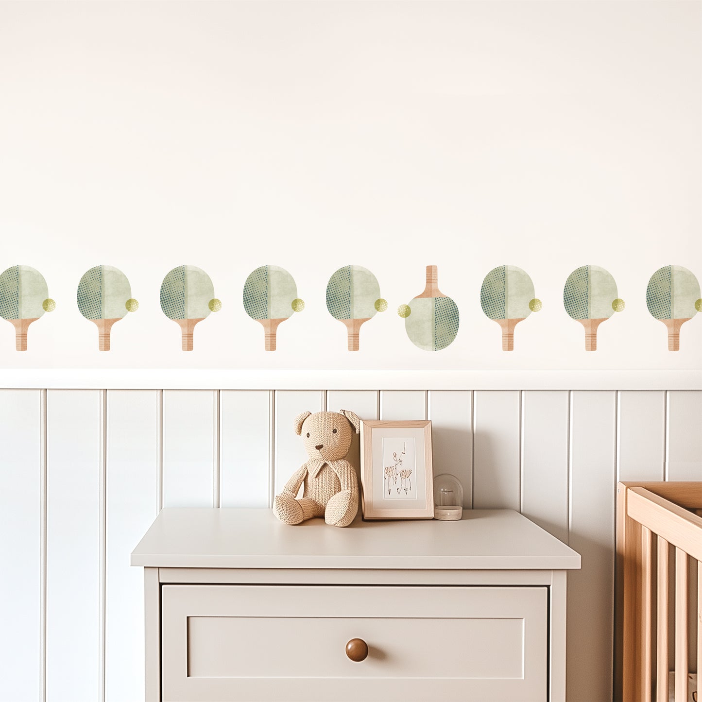 Watercolor ping pong paddles with balls removable decals by Mej Mej are placed in a row above a chair railing in a child’s playroom. 