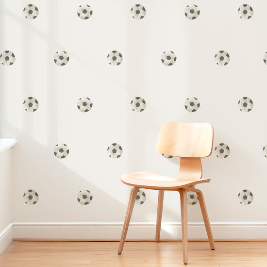 A wall is decorated with removable fabric wall decals of soccer balls by Mej Mej. They are placed in a modern grid pattern. A mid-century chair sits in front of them for scale.