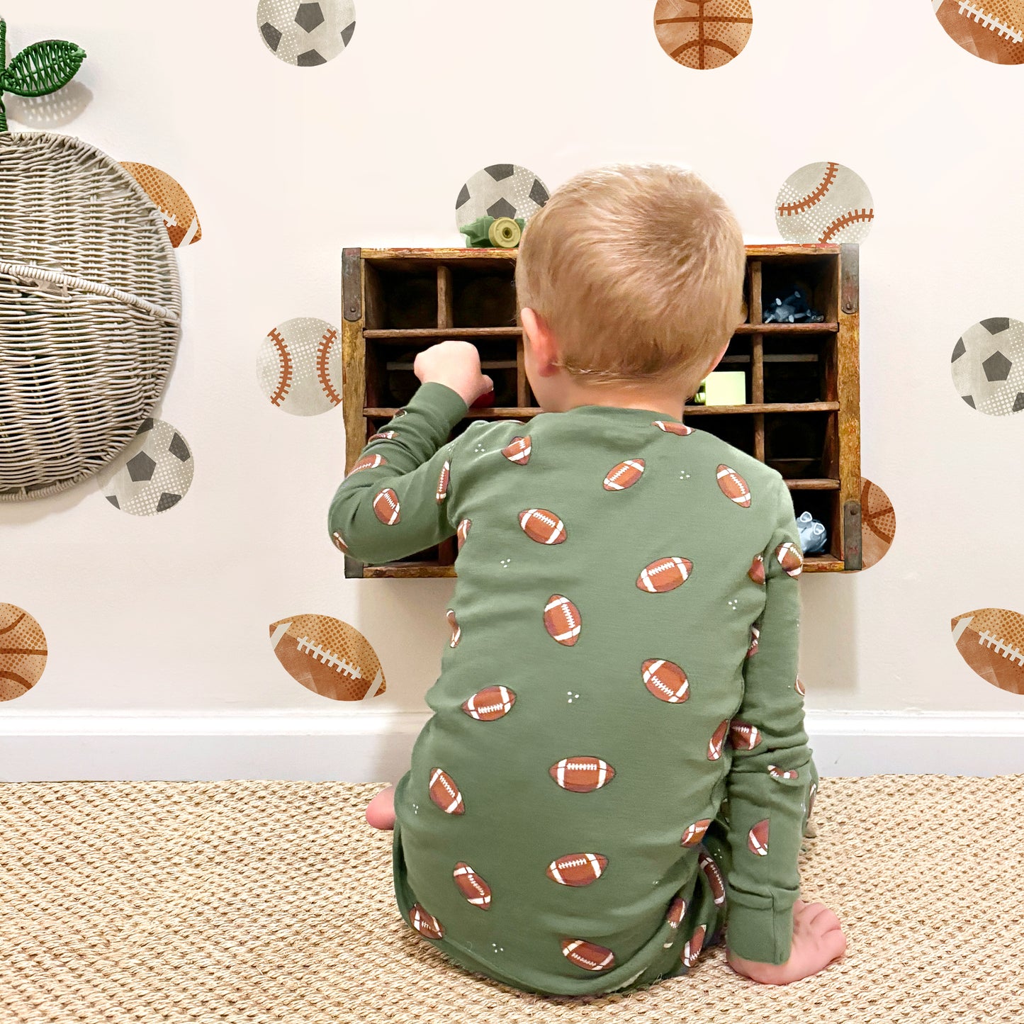 A child plays with toys in a shelf in front of a wall adorned with watercolor Sports Balls Wall Decals by Mej Mej.