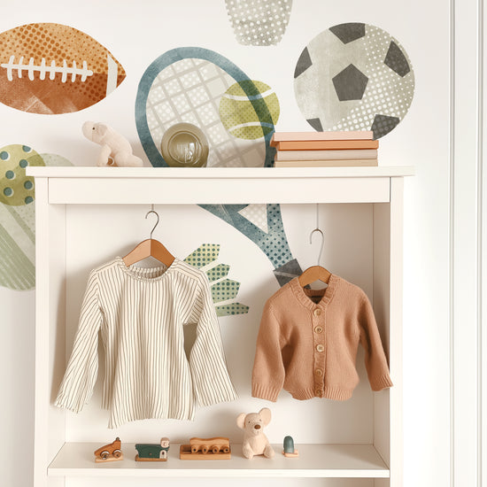 Removable fabric wall decals by Mej Mej are the backdrop for a contemporary white open-backed shelf unit with cute children’s clothes hanging on wooden hangers.