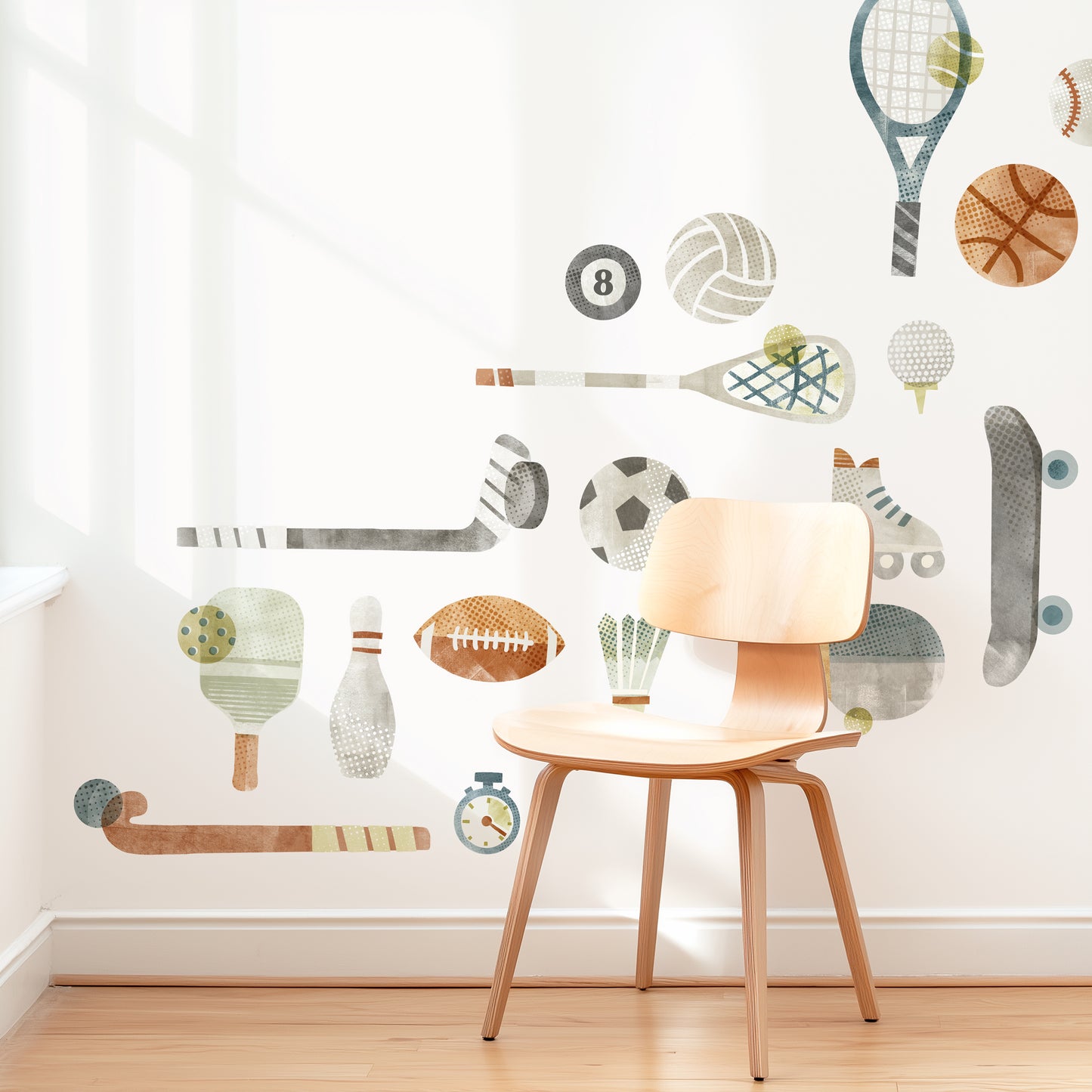 A modern space is decorated with removable fabric wall decals of all different sports equipment designed with textural watercolor artwork by Mej Mej. They are placed in an angular grid pattern. A mid-century chair sits in front of them for scale.