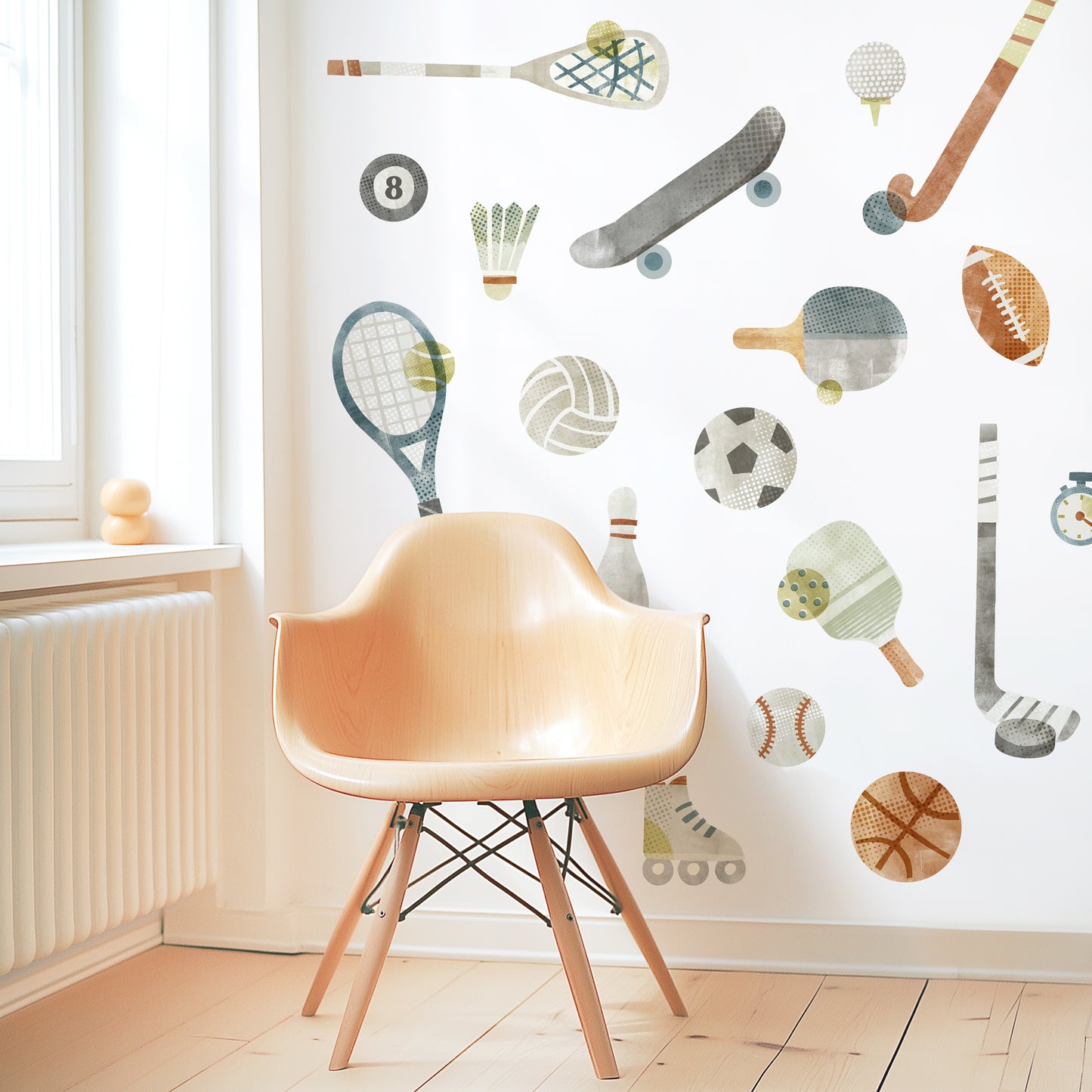 A modern space is decorated with removable fabric wall decals of all different sports equipment designed with textural watercolor artwork by Mej Mej. They are placed in an open pattern. A modern chair sits in front of them for scale.