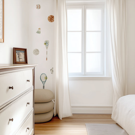 Removable fabric wall decals of sports equipment are arranged in toss pattern on an accent wall in a sun-filled teen’s room.