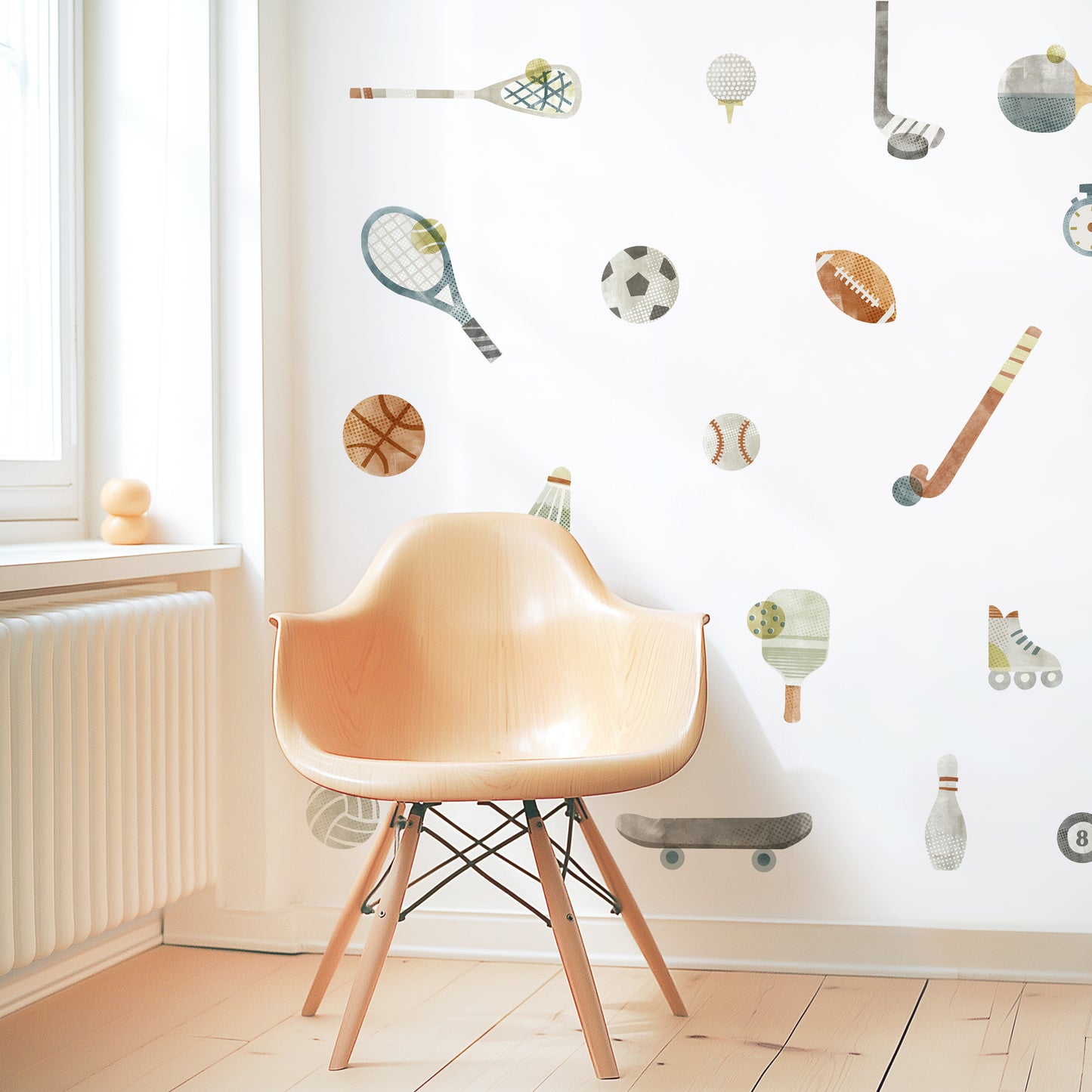 A modern space is decorated with removable fabric wall decals of all different sports equipment designed with textural watercolor artwork by Mej Mej. They are placed in an open pattern. A modern chair sits in front of them for scale.