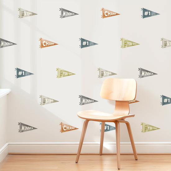 A wall is decorated with removable fabric wall decals of sports pennants by Mej Mej. They are placed in a modern grid pattern. A mid-century chair sits in front of them for scale.