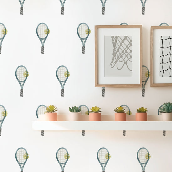 An even grid of watercolor tennis rackets wall decals by Mej Mej adorns a wall in a sunny room. A narrow shelf hangs displaying succulents.