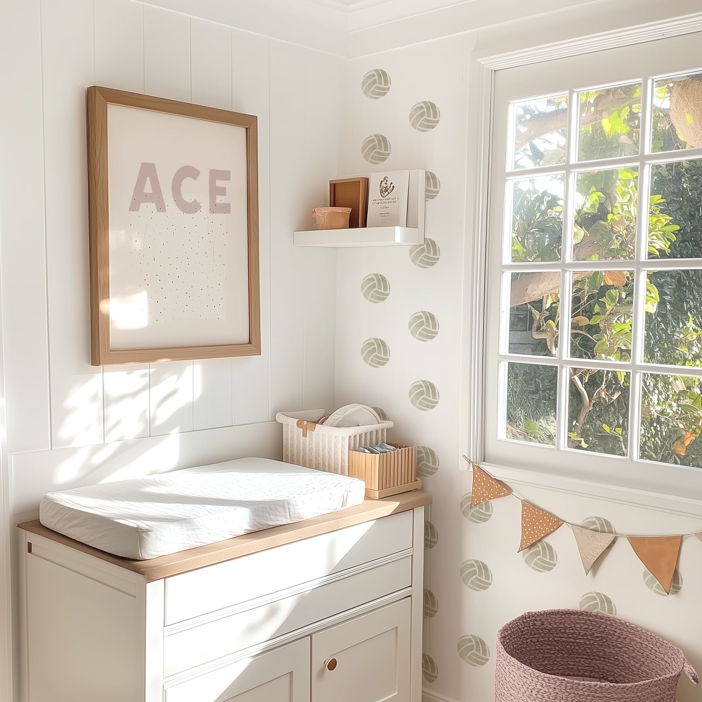 Watercolor volleyball decals by Mej Mej are placed in a grid pattern on an accent wall in a sunlit child’s nursery. A changing table is in front of the accent wall with a framed print that says ACE.